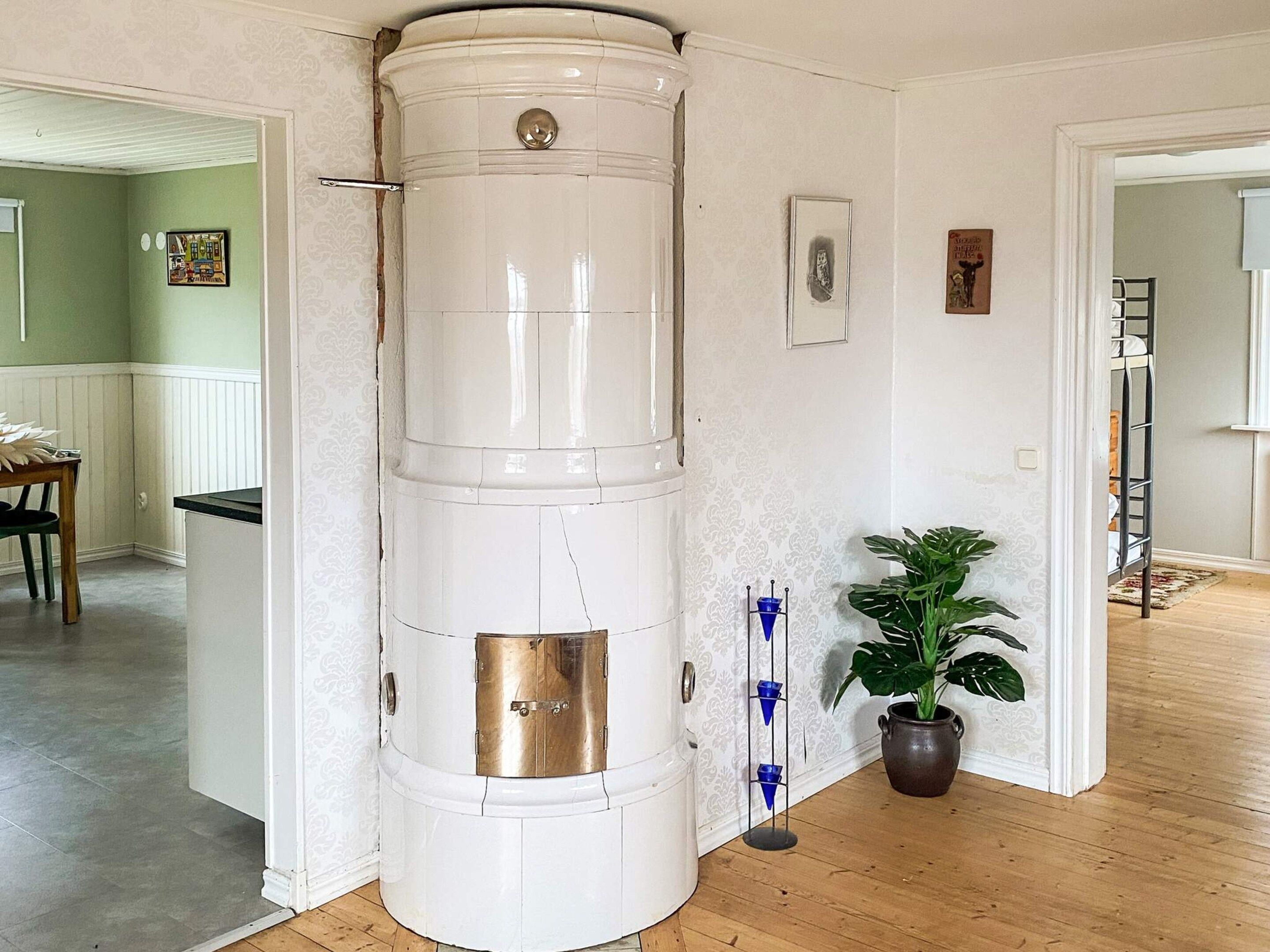 Un rincón con un objeto cilíndrico blanco, una planta en maceta y una puerta que da a otra habitación.