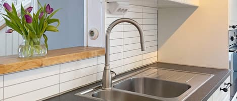 A kitchen with a stainless steel sink, white tiled backsplash, and a wooden countertop.