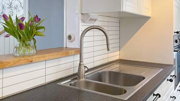 A kitchen with a stainless steel sink, a wooden countertop, and a vase with purple flowers.