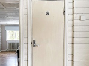 Une porte de couleur beige avec une pancarte indiquant « WC », un radiateur et une fenêtre avec des rideaux.