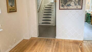 A hallway with a wooden floor, a staircase, and two framed pictures on the walls.