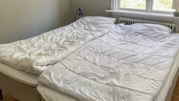 A double bed with white bedding in a room with a window and a radiator.