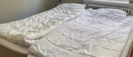 A double bed with white bedding in a room with a window and a radiator.