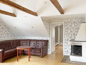 Um espaço de estar estilo loft com vigas de madeira aparentes, um sofá seccional de couro marrom, uma pequena mesa redonda e uma lareira.