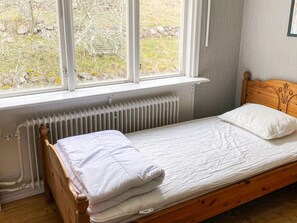 A single bed with a wooden headboard, white bedding, and a view of a garden through a window. - 8 Person Holiday Home in Anneby (Aneby)