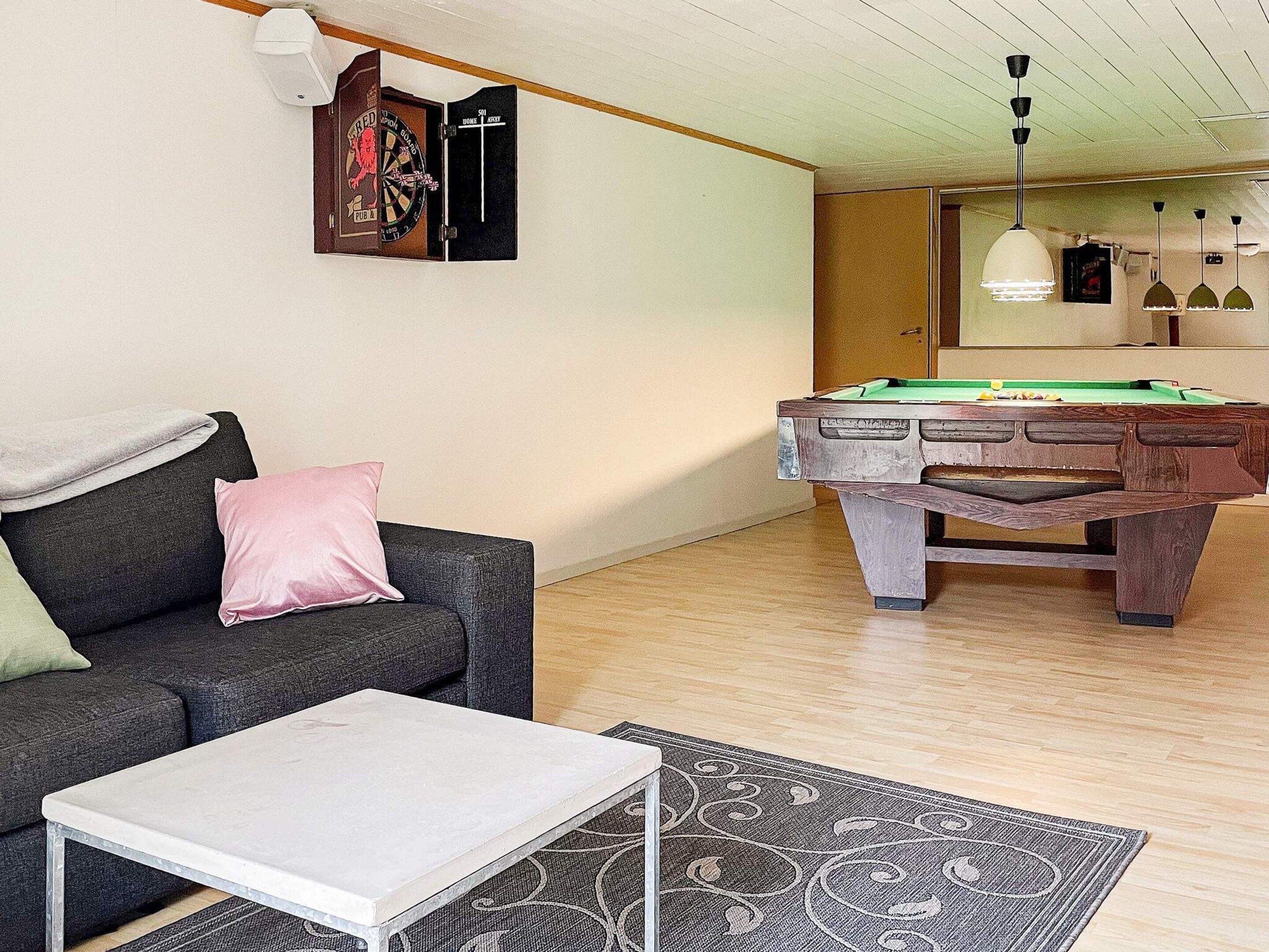 A room with a pool table, a sofa, a coffee table, and a dartboard.
