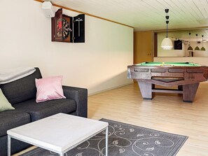 A room with a pool table, a sofa, a coffee table, and a dartboard.