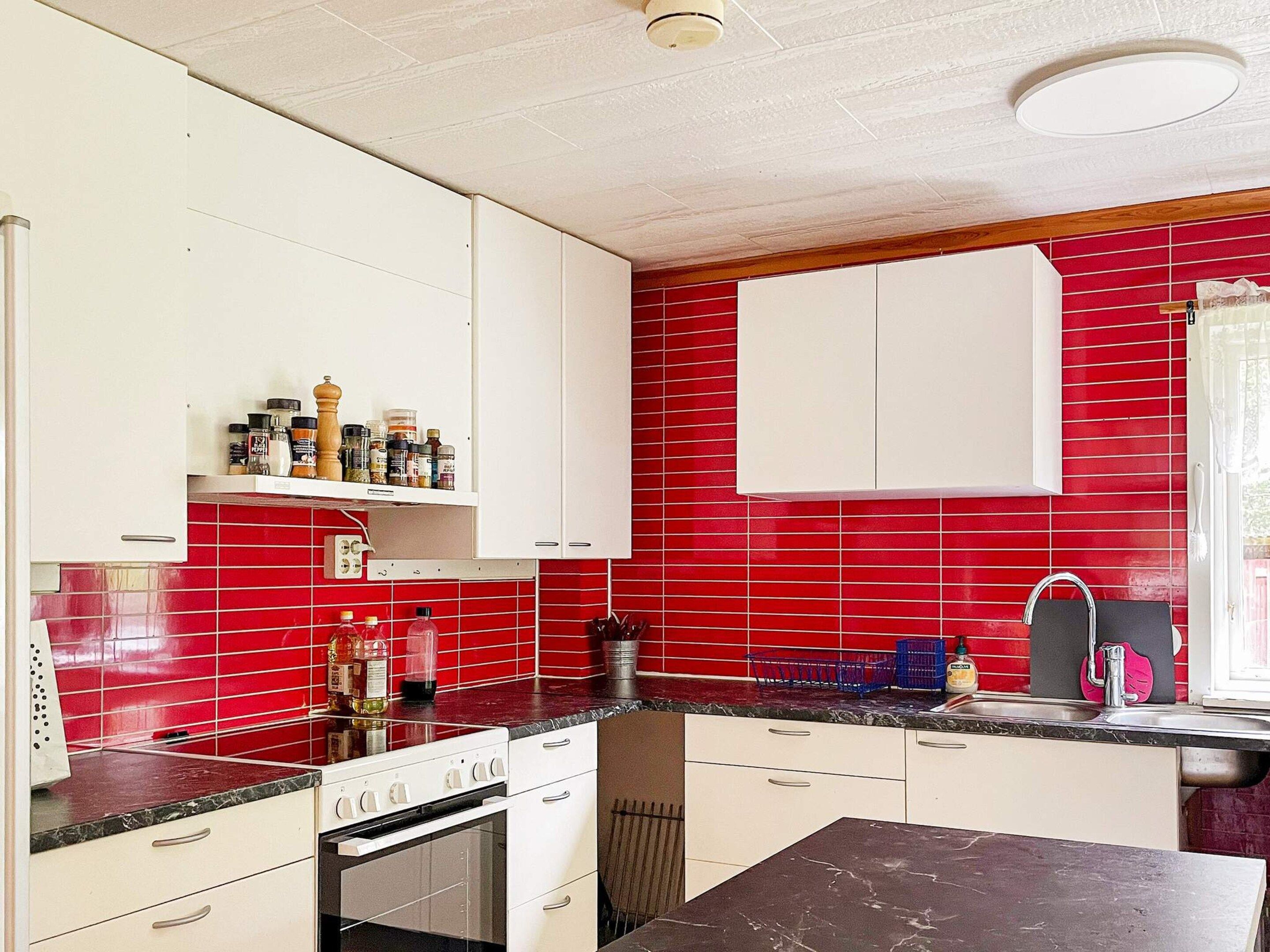 A kitchen with white cabinets, red tiled backsplash, and a black countertop.