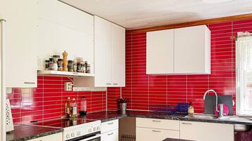 A kitchen with white cabinets, red tiled backsplash, and a black countertop.