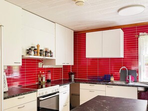 A kitchen with white cabinets, red tiled backsplash, and a black countertop.