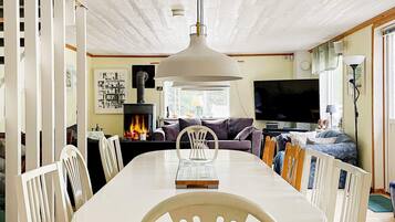 A dining area with a white table and chairs, a fireplace, a sofa, and a television.