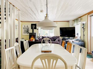 A dining area with a white table and chairs, a fireplace, a sofa, and a television.
