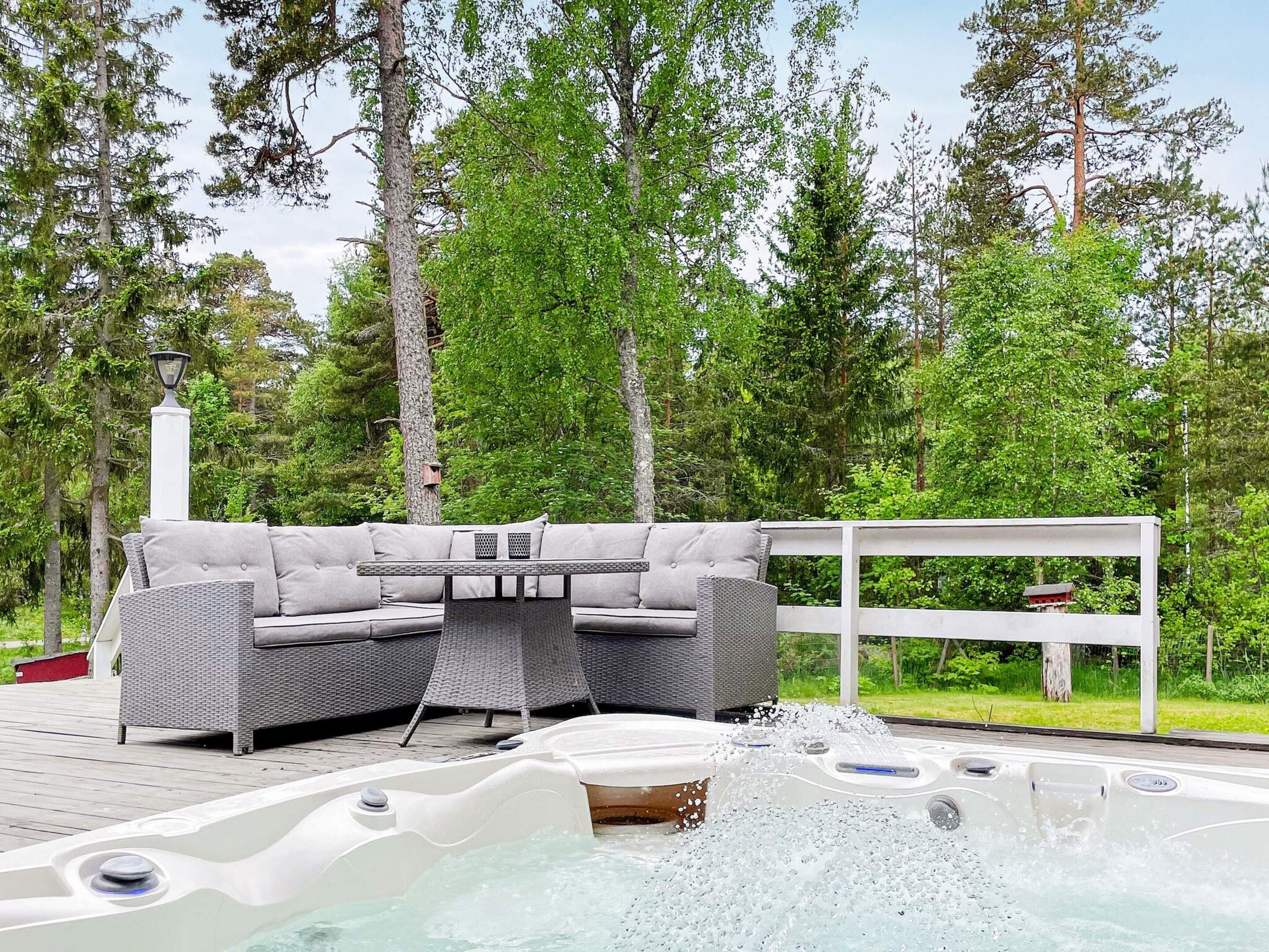 An outdoor hot tub area with a sofa and table, surrounded by trees.