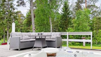 An outdoor hot tub area with a sofa and table, surrounded by trees.