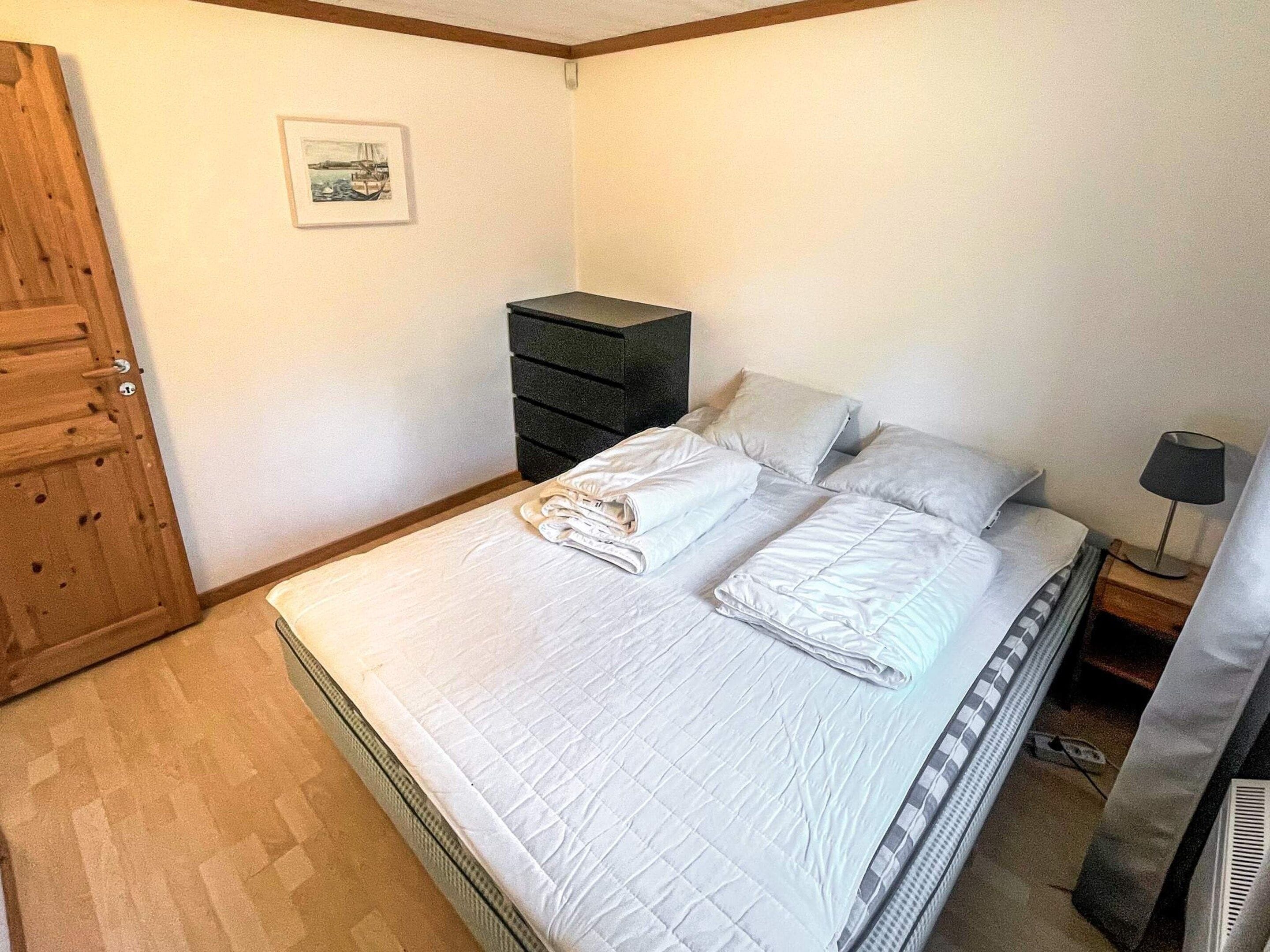 A bedroom with a bed, a dresser, a nightstand, a lamp, and a door.