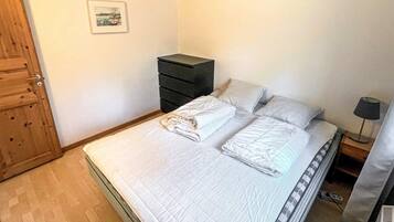 A bedroom with a bed, a dresser, a nightstand, a lamp, and a door.