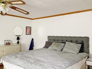 Ein Schlafzimmer mit einem Bett, einem Nachttisch, einer Lampe, einem Spiegel und einem Deckenventilator.