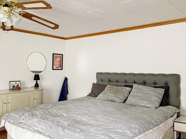 A bedroom with a bed, a bedside table, a lamp, a mirror, and a ceiling fan.