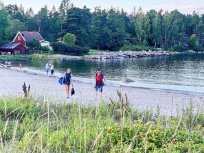 A lakeside walkway with people walking, surrounded by greenery and a house in the background.