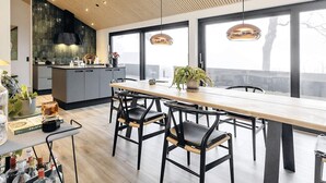 A modern kitchen with a wooden ceiling, large windows, and a dining area with a long table and chairs. - 5 Star Holiday Home in Frederikshavn (Frederikshavn)