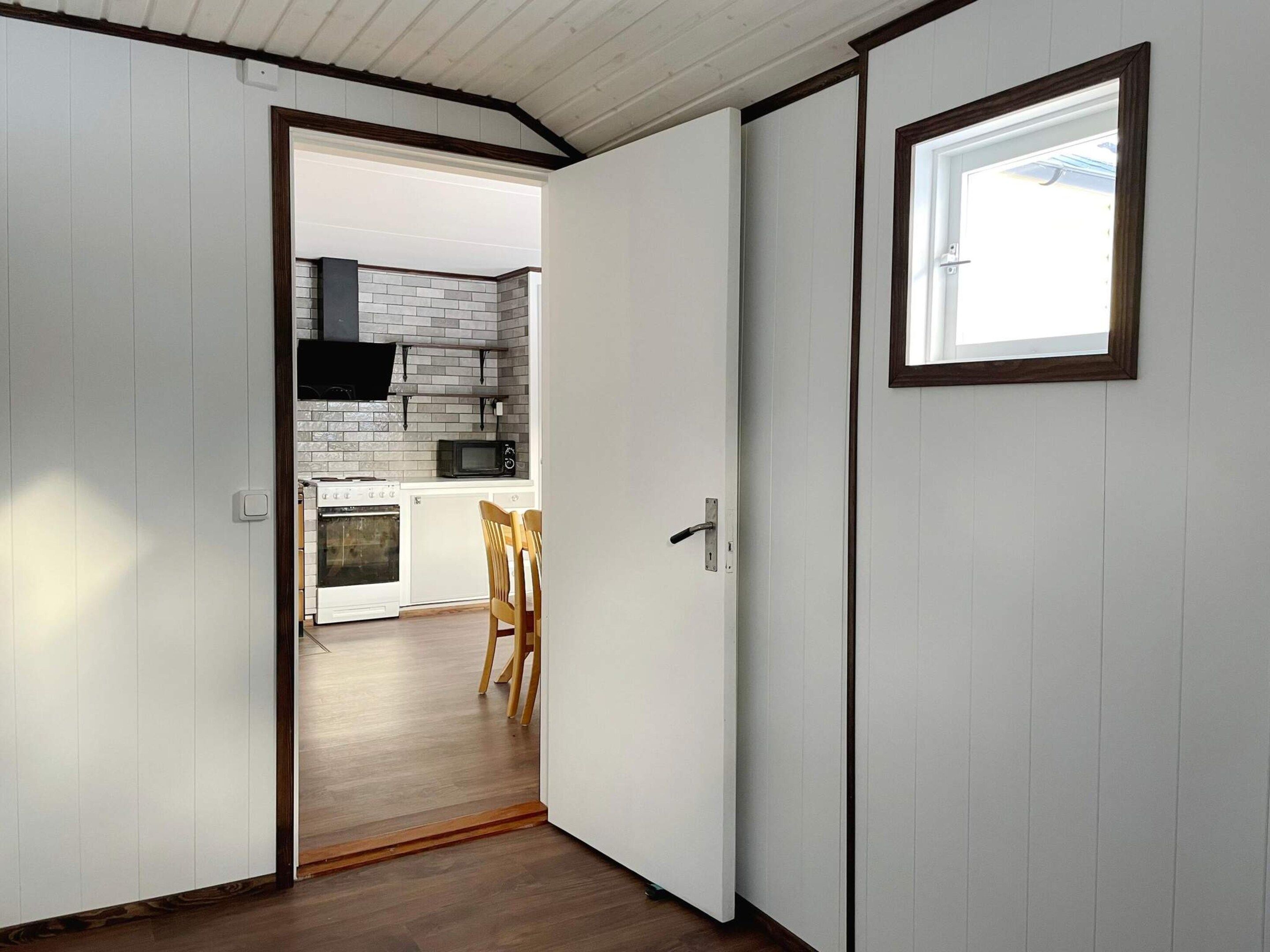 A narrow hallway leading to a kitchen with white cabinets, a microwave, and a stove.