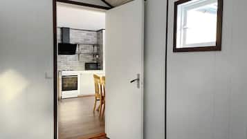 A narrow hallway leading to a kitchen with white cabinets, a microwave, and a stove.