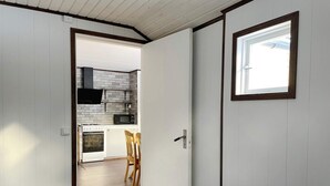 Un couloir étroit mène à une cuisine équipée de meubles blancs, d’un four à micro-ondes et d’une cuisinière.
