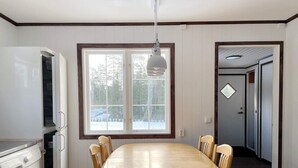 Une cuisine équipée d’un lave-linge intégré, une table à manger avec des chaises, une fenêtre donnant sur les arbres et une porte menant à une autre pièce.