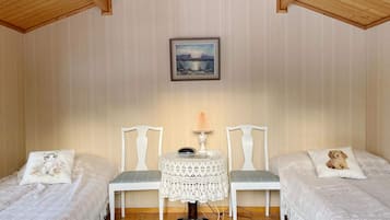 A cozy room with two single beds, a small table with a lamp, and a framed picture on the wall.