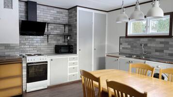 A compact kitchen with a microwave, stove, and oven, a dining table with chairs, and pendant lights above.