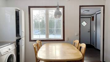 A kitchen with a built-in washing machine, a dining table with chairs, and a window with a view of trees.