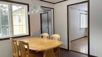 A dining area with a wooden table and chairs, white walls, and a door leading to another room.