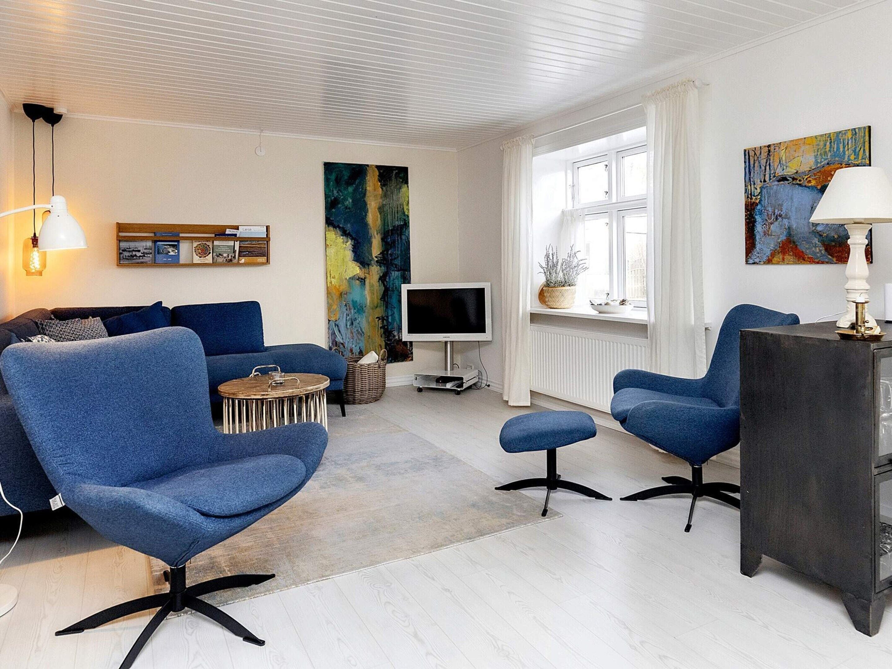 Een moderne woonkamer met een bank, twee fauteuils, een televisie en kunstwerken aan de muren.