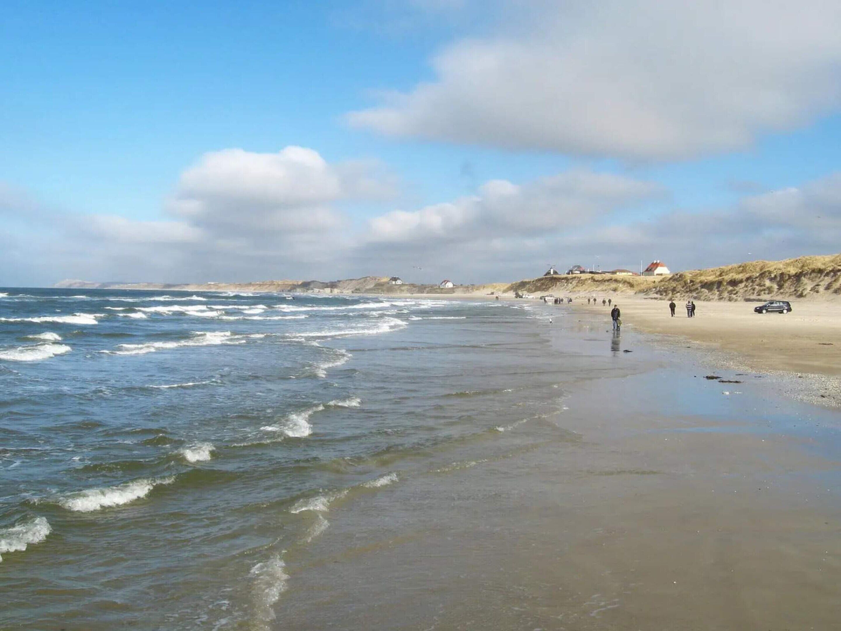Une plage avec des vagues, une étendue de sable et quelques personnes qui se promènent.