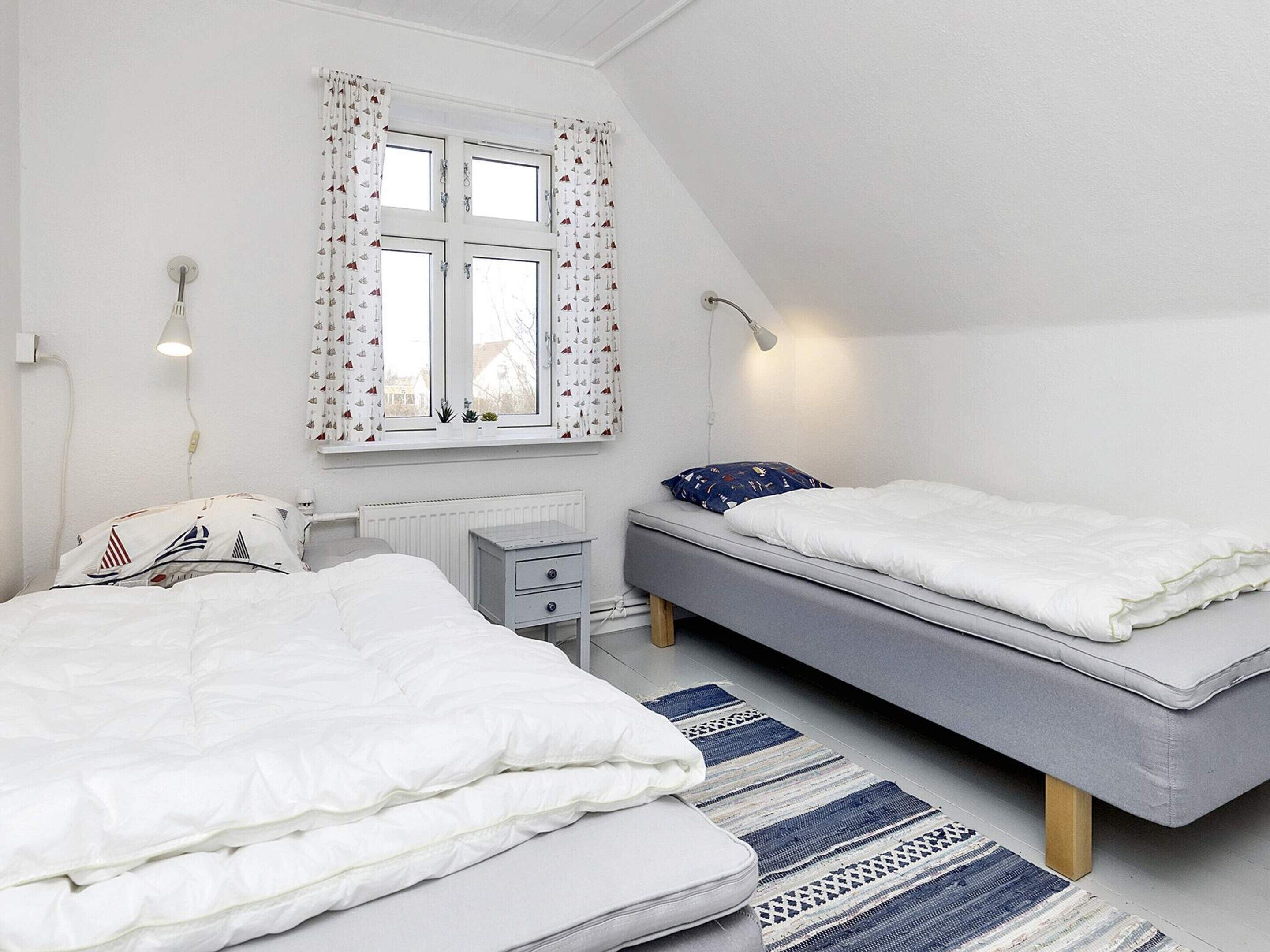 Una camera da letto con due letti, una finestra con tende, un comodino e una lampada.