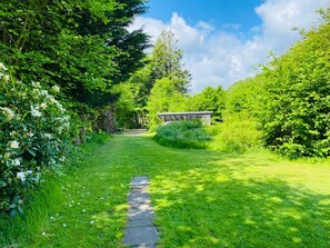 A garden pathway leading to a wooden structure, surrounded by lush greenery and trees. - 6 Person Holiday Home in Bogense (Bogense)