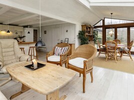 A spacious living area with a wooden dining table, wicker chairs, and a large window offering a view of the outdoors.