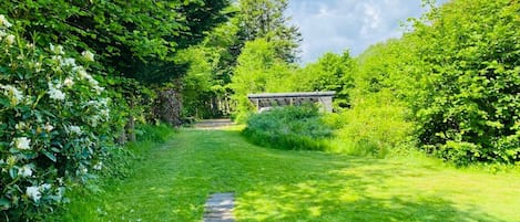 Un sendero de jardín que lleva a una estructura de madera, rodeada de exuberante follaje y árboles.