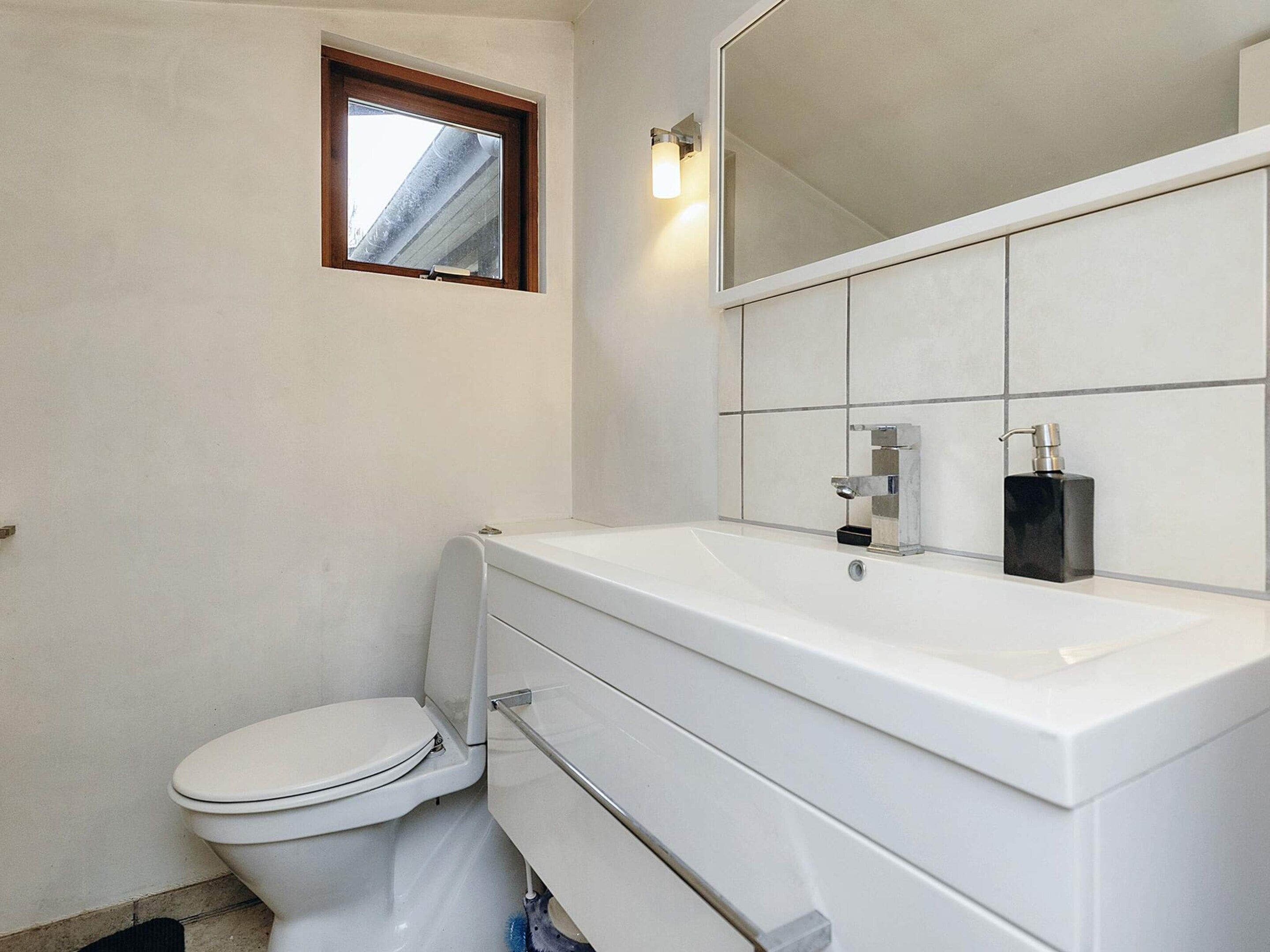 Un bagno con un water, un lavandino con uno specchio sopra e una finestra sopra il water.