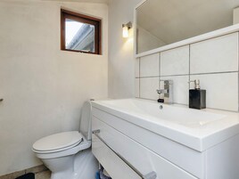 A bathroom with a toilet, a sink with a mirror above it, and a window above the toilet.
