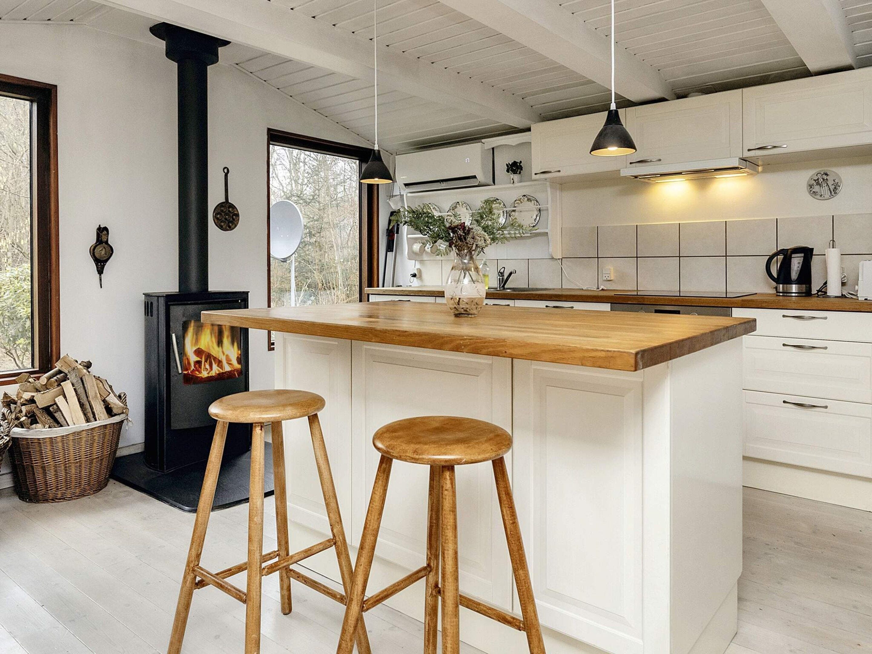 Una cocina moderna con una isla central, taburetes de madera, estufa integrada y armarios blancos.
