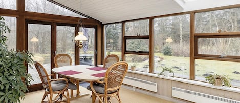 A sunroom with a dining table and chairs, large windows, and a hanging light fixture.