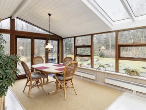 A sunroom with a dining table and chairs, large windows, and a hanging light fixture. - 6 Person Holiday Home in Bogense (Bogense)