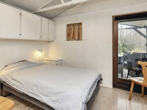 A bedroom with a bed, a bedside table, a wall-mounted light, a wooden chair, and a sliding glass door leading to an outdoor area with furniture. - 6 Person Holiday Home in Bogense (Bogense)