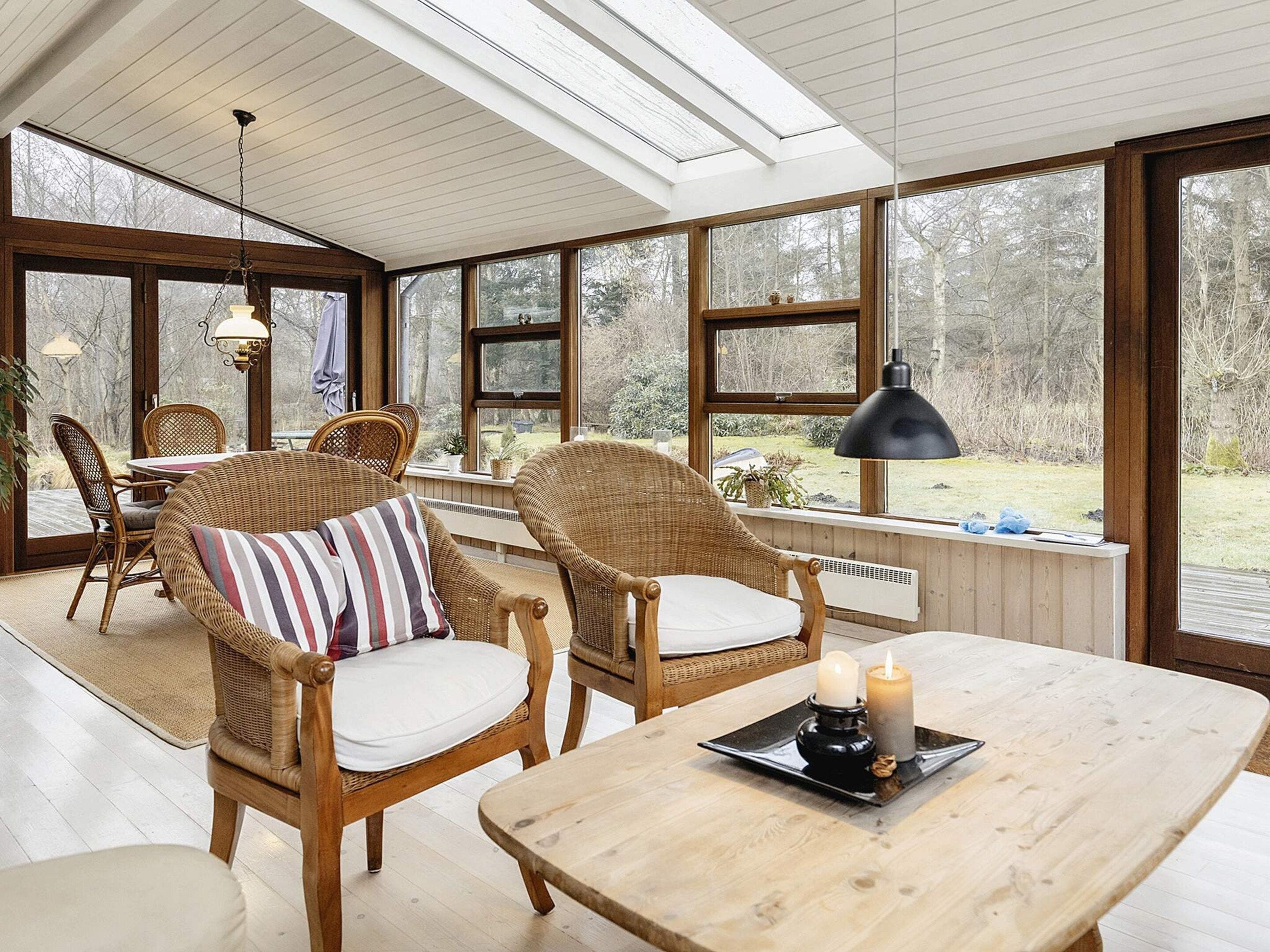 A cozy room with wicker furniture, a table with candles, and large windows offering a view of the outdoors.