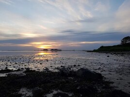 A beach with a sunset, rocky foreground, and distant landmass.