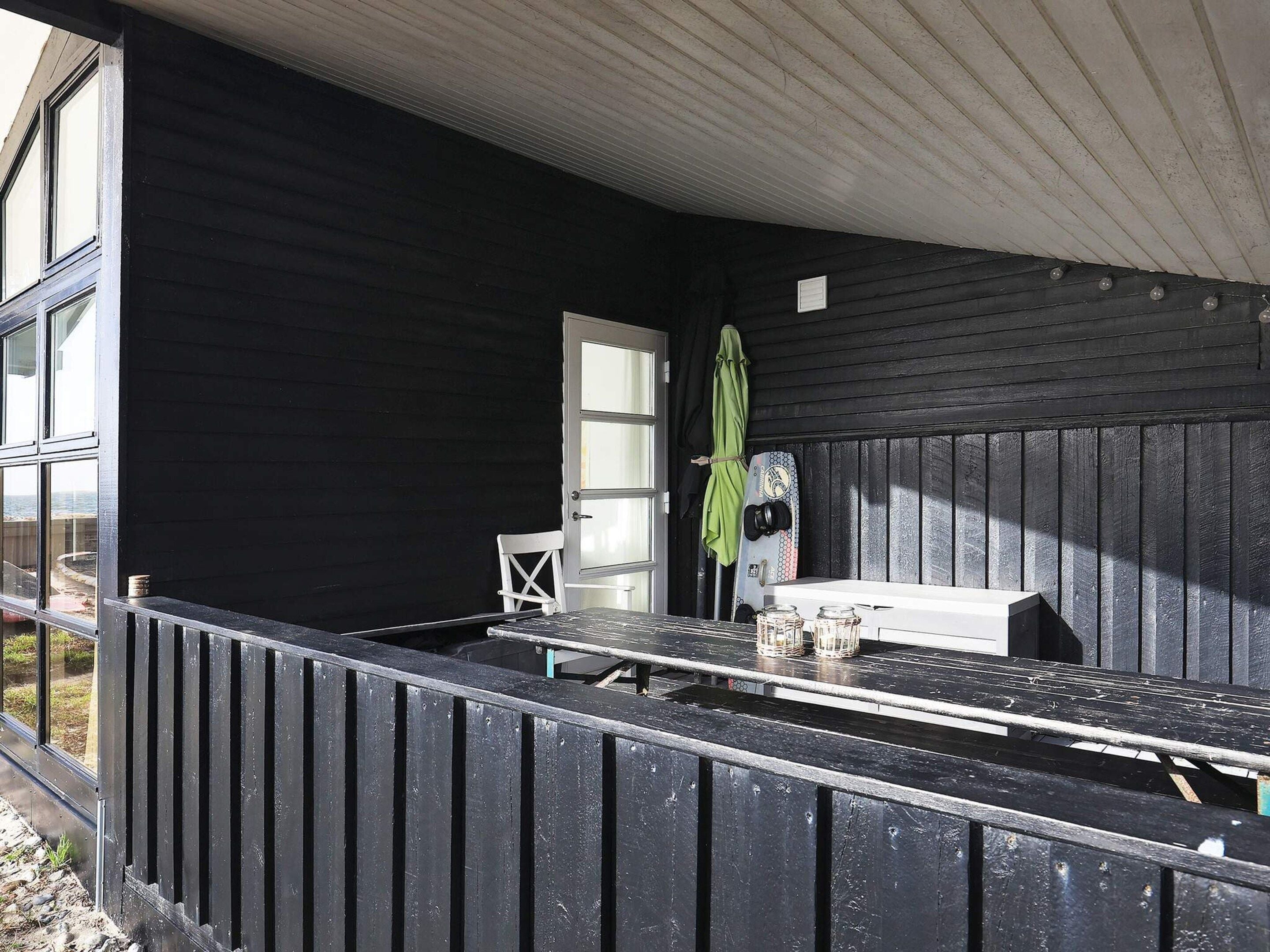 A covered outdoor seating area with a table and chairs, a door, and a window.