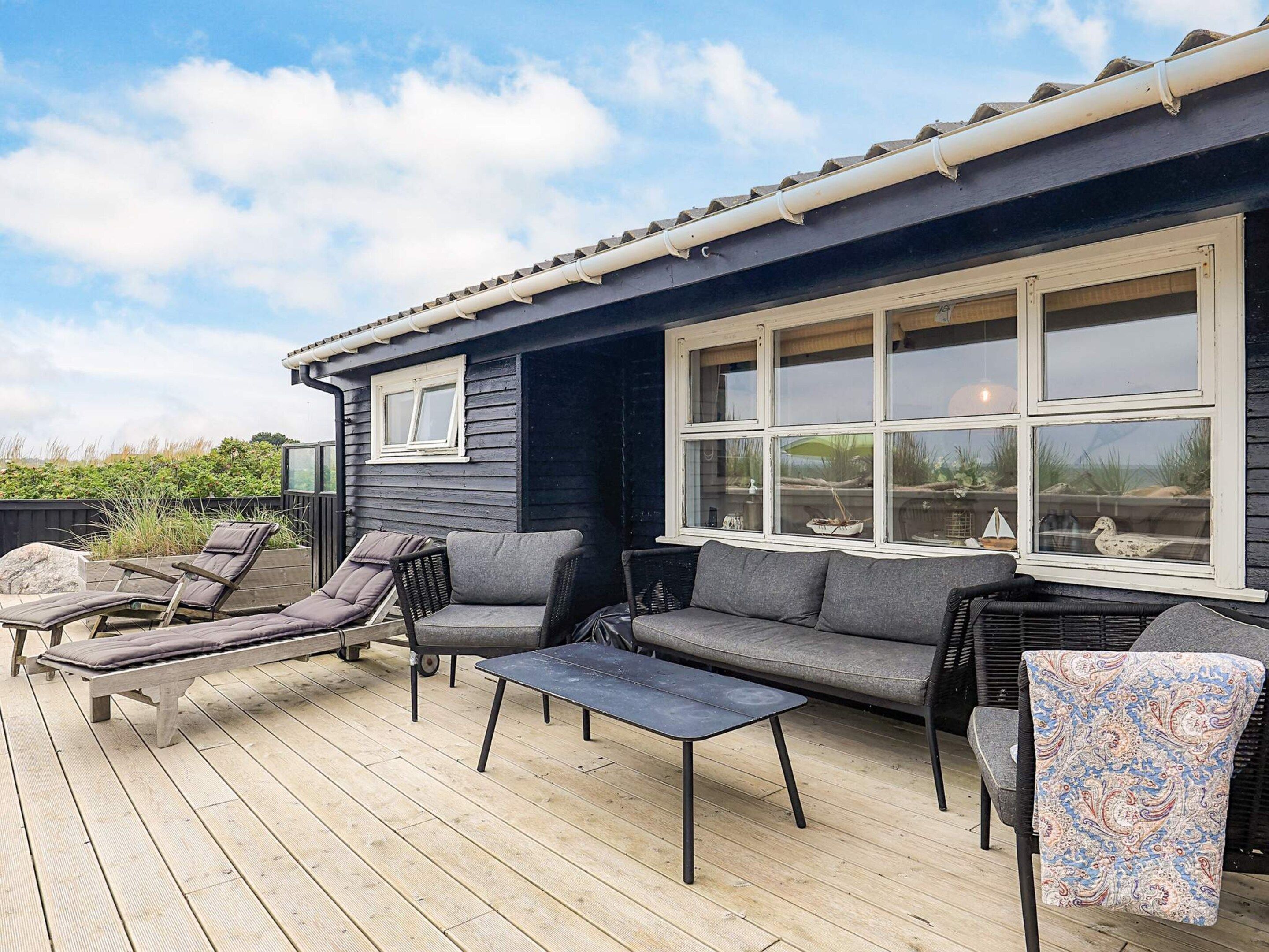 Una terraza con mobiliario exterior, incluyendo sillones reclinables y un sofá, un ventanal con múltiples paneles y vistas del paisaje circundante.