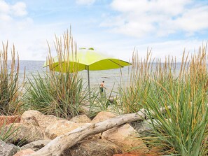 A beach with a person walking under a green umbrella, surrounded by rocks and tall grass. - 4 Star Holiday Home in Karrebaeksminde (Karrebæksminde)