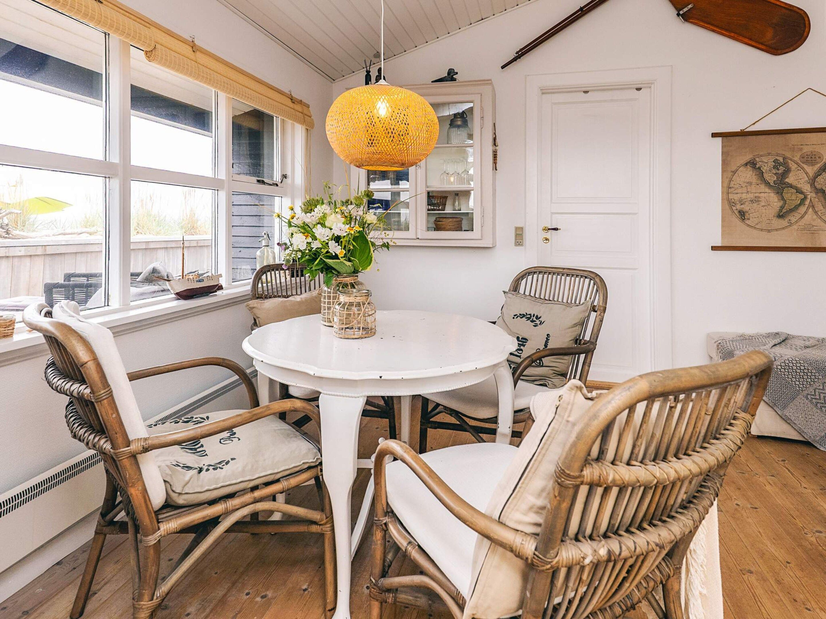 A dining area with wicker chairs, a round white table, and a hanging yellow lamp.